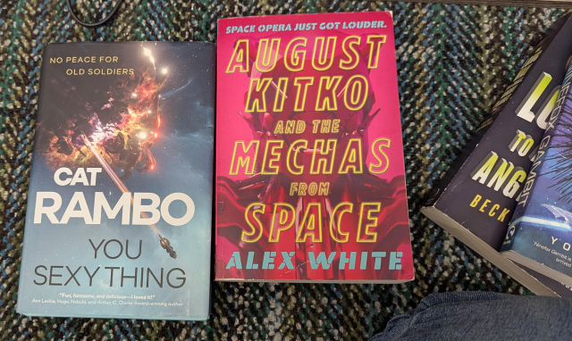 Two paperback books on a carpet: Cat Rambo’s You Sexy Thing and Alex White’s August Kitko and the Mechas from Space