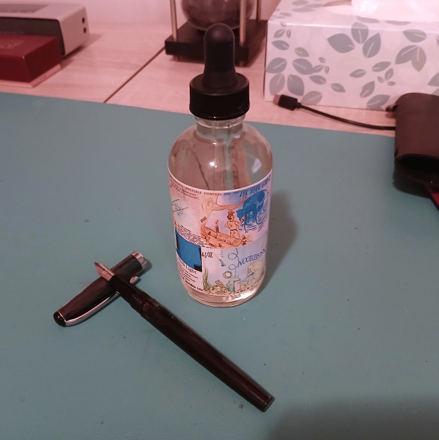 The aforementioned ink and pen.  The ink is a large bottle with a translucent yellow-ish ink (which when used is only visible under UV light).  The pen is a slim eye dropper pen.  The pen is uncapped and placed with the nib end propped up on the cap to be all fancy looking and stuff.